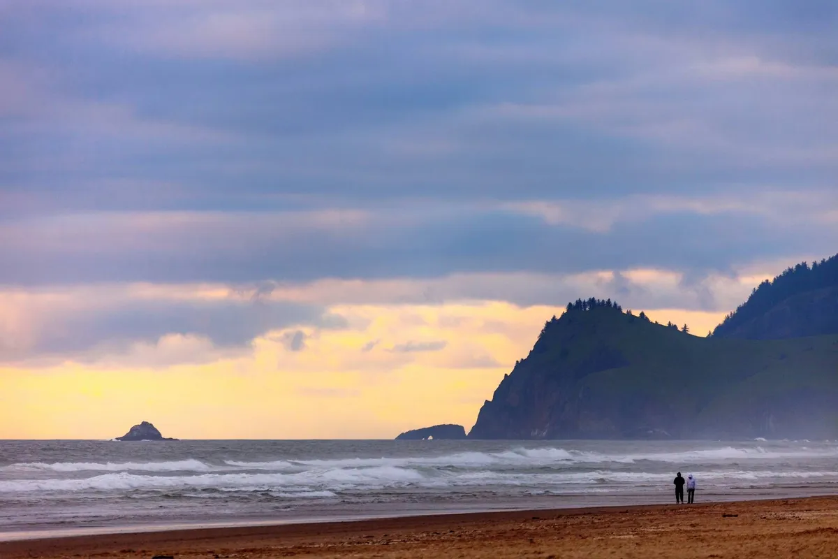 A tranquil beach scene at sunset, with a couple walking hand-in-hand along the shoreline. The ocean waves gently lap the sand, and warm hues light up the sky, creating a distinctly romantic and peaceful atmosphere.