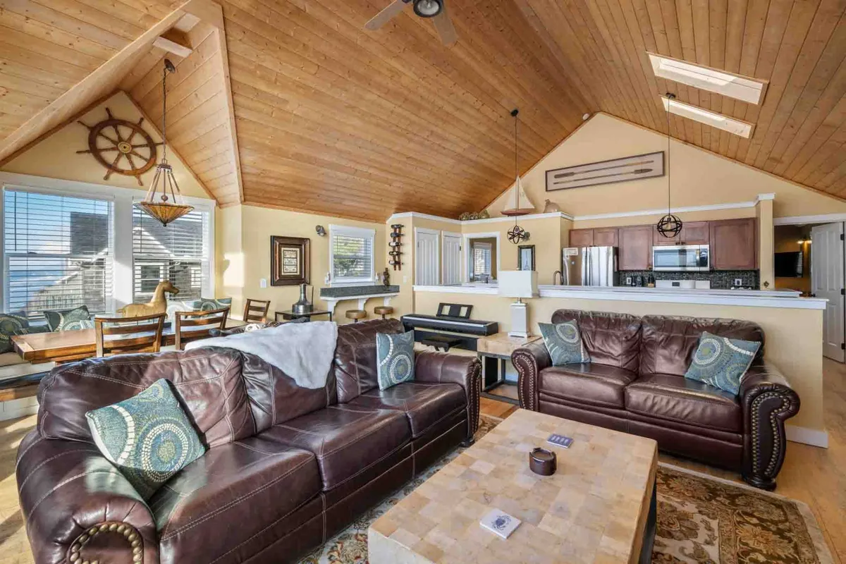 A welcoming, open-plan living and dining space featuring plush leather sofas, a wooden ceiling, and a dining area visible in the background. Nautical accents and a coffee table invite relaxation, socializing, or game nights, while sunlight streams through the windows, enhancing the cheerful atmosphere.