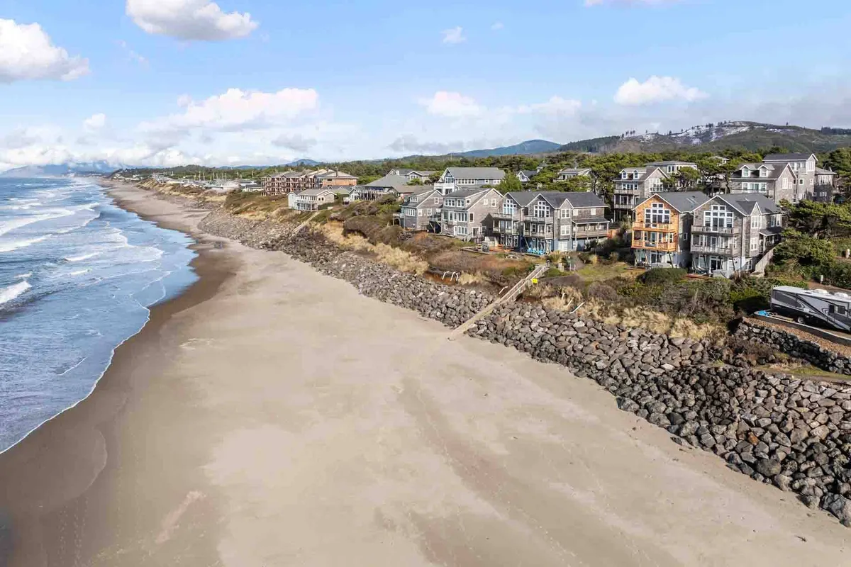 This exterior image showcases a tranquil stretch of beach with gentle ocean waves, homes lining the shore, and striking rock formations. The sand and surf invite viewers to imagine peaceful walks and moments of relaxation right outside the property.