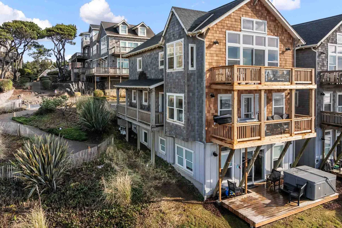 A spacious wooden balcony with a hot tub, large windows, landscaped garden, and sweeping sunset views. The spa/hot tub is the focal point, promising relaxation and intimacy in a private outdoor setting.