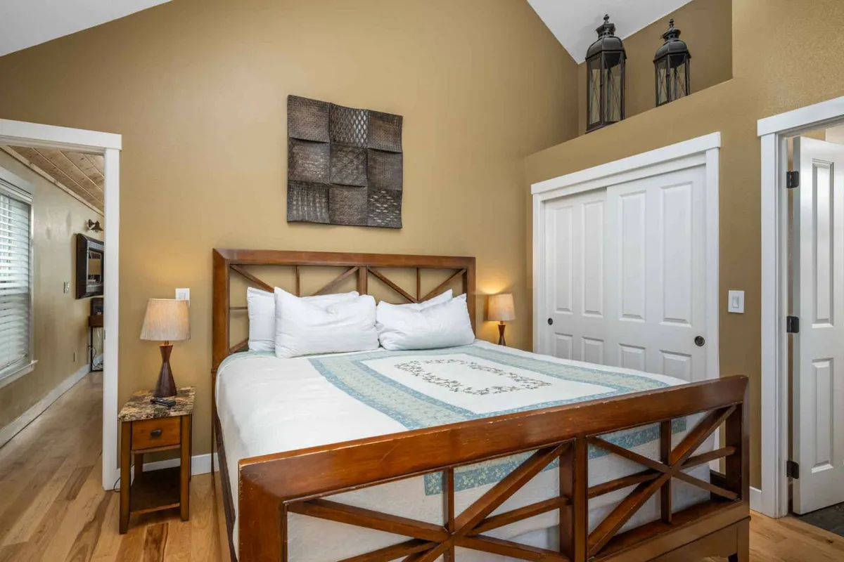 A cozy bedroom with a comfortable bed dressed in soft linens, flanked by two nightstands and decorated with soothing wall art. Gentle natural light streams through doors, creating an inviting and restful atmosphere.