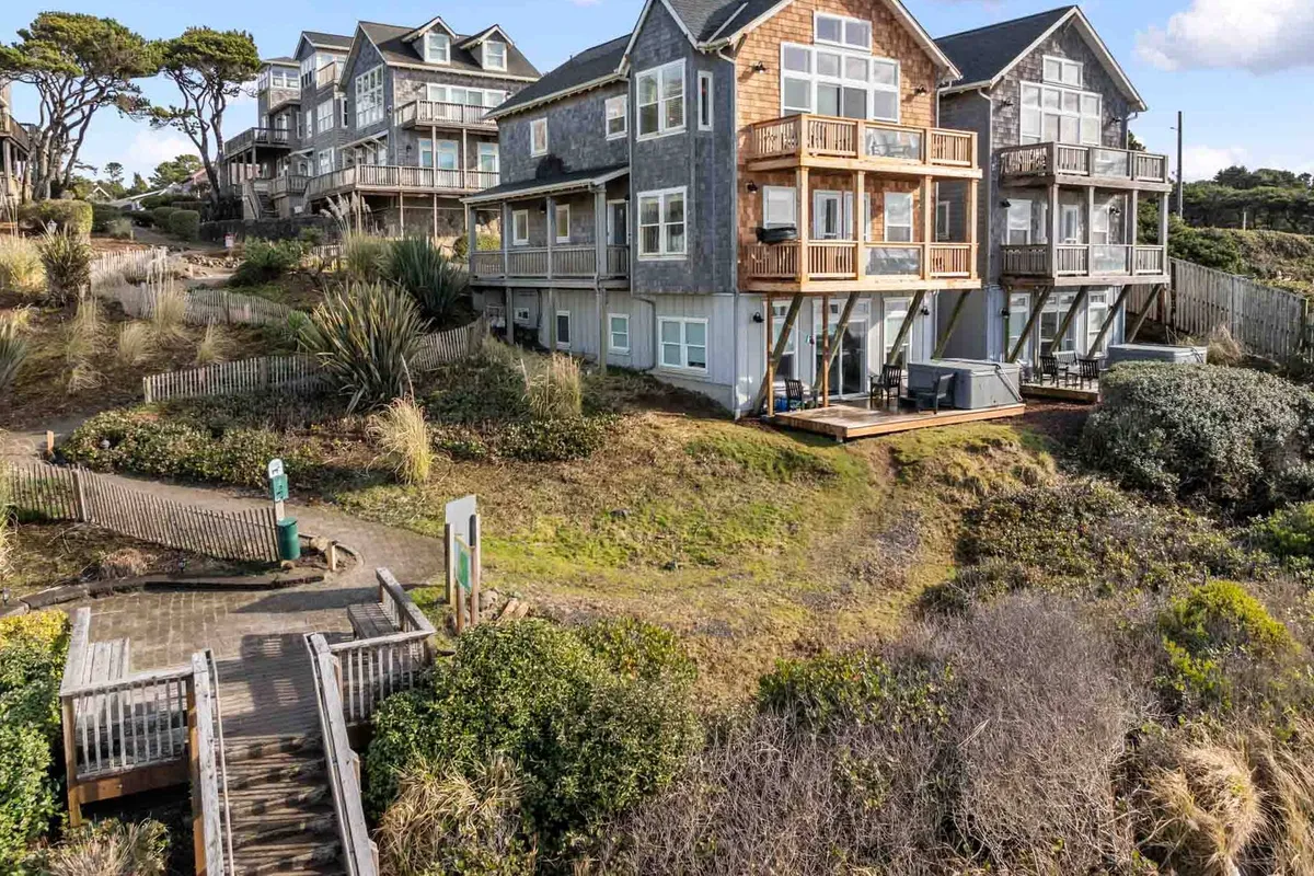 A tranquil neighborhood of multi-level coastal homes with wooden walkways winding through lush greenery, framed by the ocean in the distance. The scene suggests a quiet, respectful neighborhood perfect for peaceful walks and exploration.