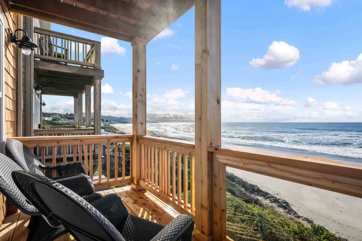 A serene deck overlooking the ocean, with comfortable chairs arranged for relaxing, watching the sunrise, or savoring a morning coffee. The wooden railing frames panoramic views of the water, inviting peaceful moments together.