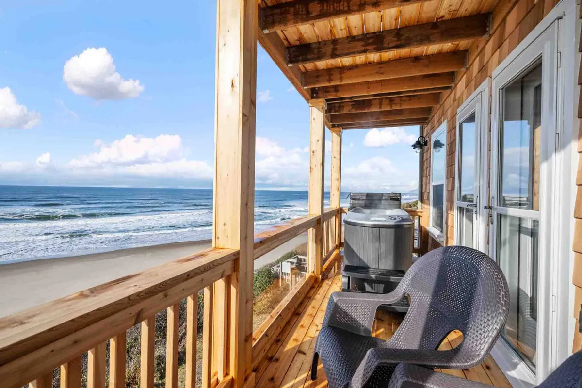 This exterior image showcases a private hot tub on a deck overlooking the Pacific Ocean. The view includes the inviting hot tub, comfortable deck furniture, and the vast ocean stretching to the horizon under the evening sky, evoking a tranquil and relaxing atmosphere.
